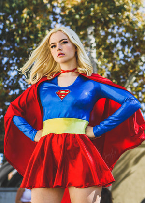 Person wearing a Superman costume with a red cape and blue shirt in an outdoor setting.