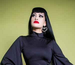 Woman wearing a black top with wide sleeves and black boots on a green background